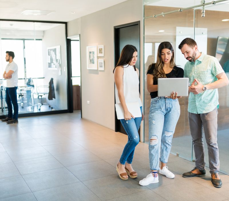 Business colleagues discussing ideas over laptop in office corridor
